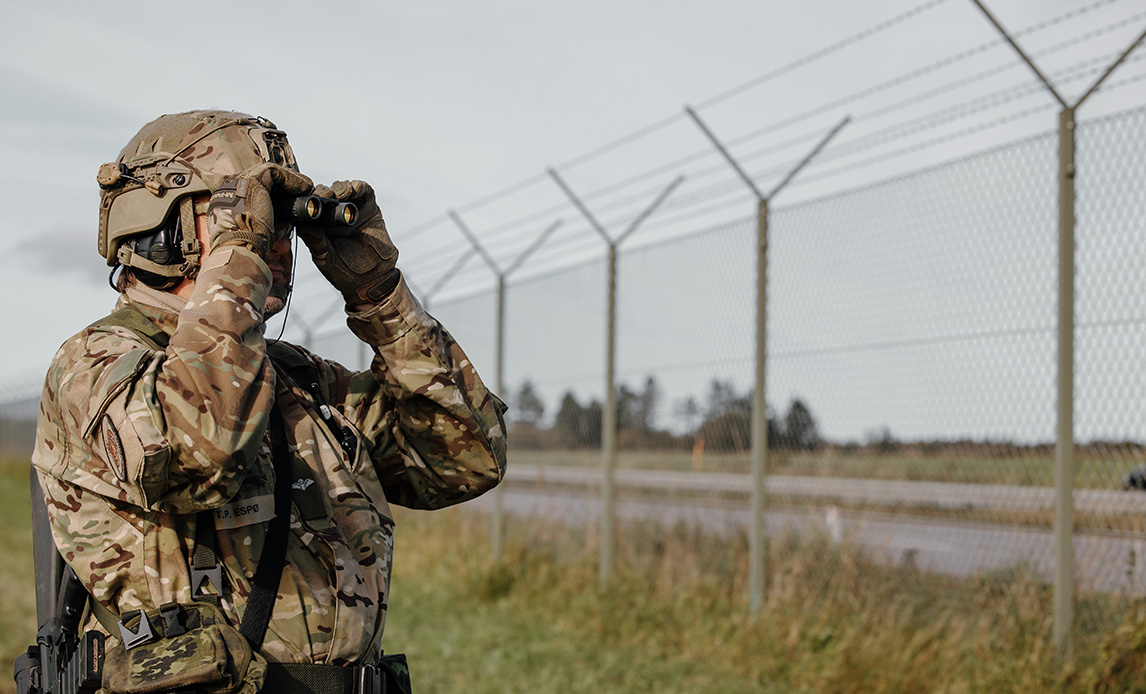 Soldat spejder ud over en flyvestation med en kikkert