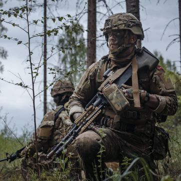 Soldat sidder på hug i skov.